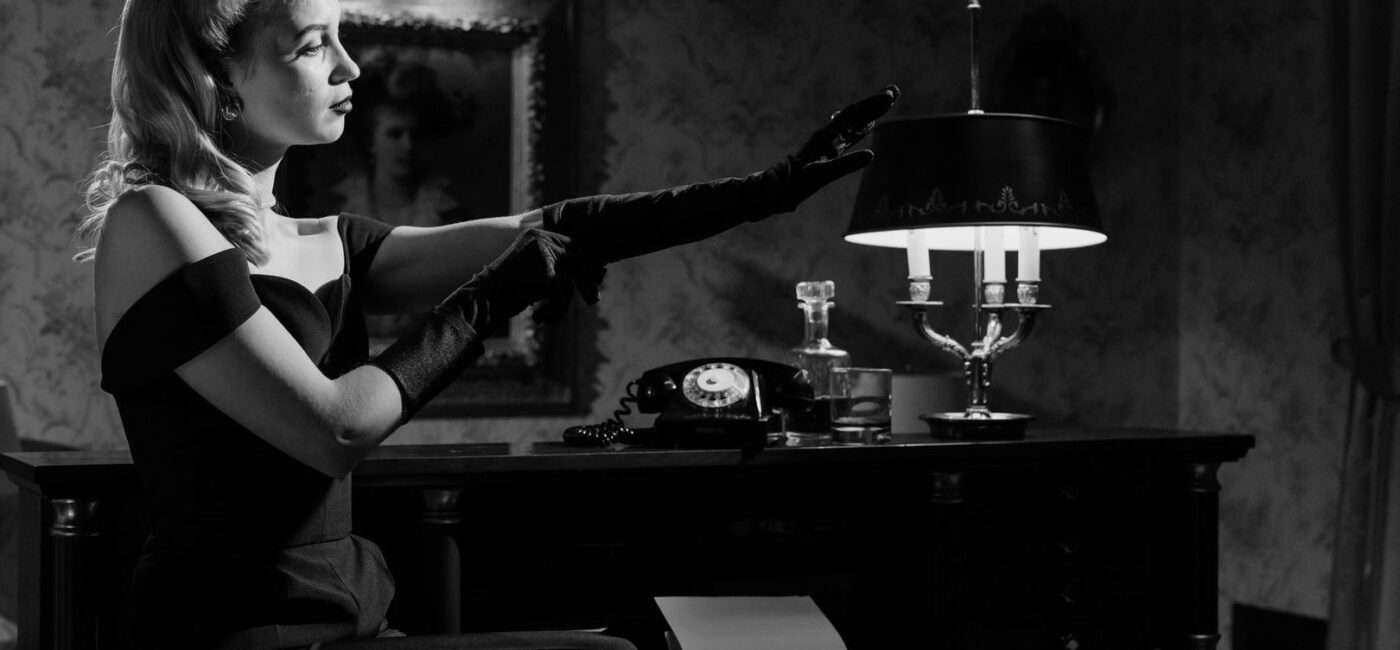 Black-and-white woman in gloves reaching across a desk with a typewriter