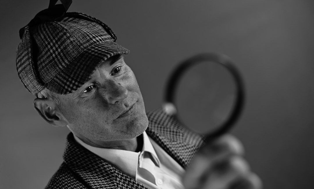 Black-and-white portrait of a detective examining a magnifying glass